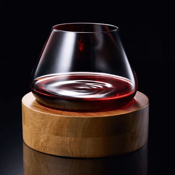 Rotating crystal wine glass on round wooden coaster, filled with red wine