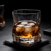 Crystal whiskey tumbler with amber drink and scattered ice on coaster