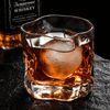 Crystal tumbler whiskey glass with amber liquor and ice, faceted sides