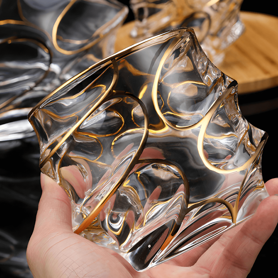 Handheld view of clear crystal whisky glass with raised gold line swirl pattern