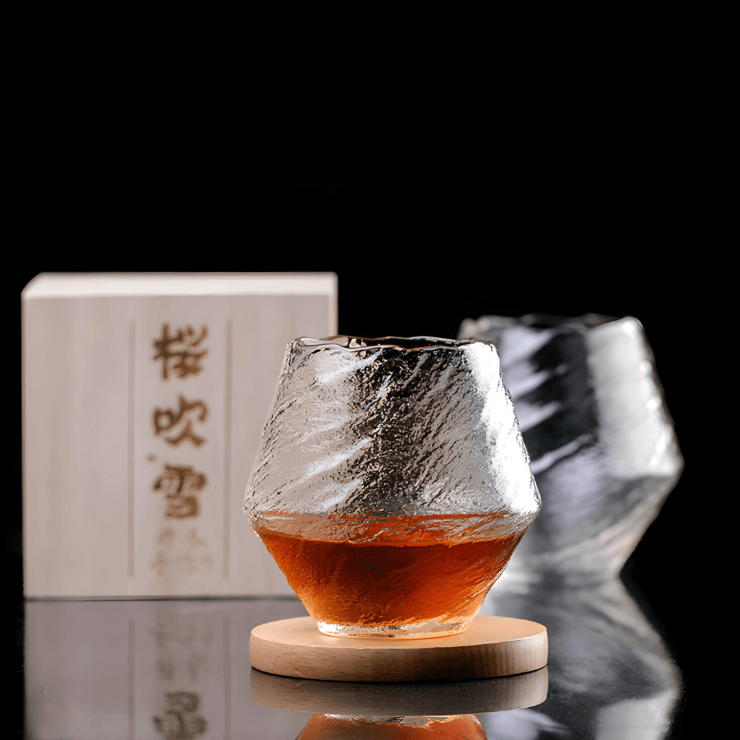 Crystal whisky glass with amber liquid on wood coaster, faceted clear smoky glass