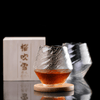 Crystal whisky glass with amber liquid on wood coaster, faceted clear smoky glass
