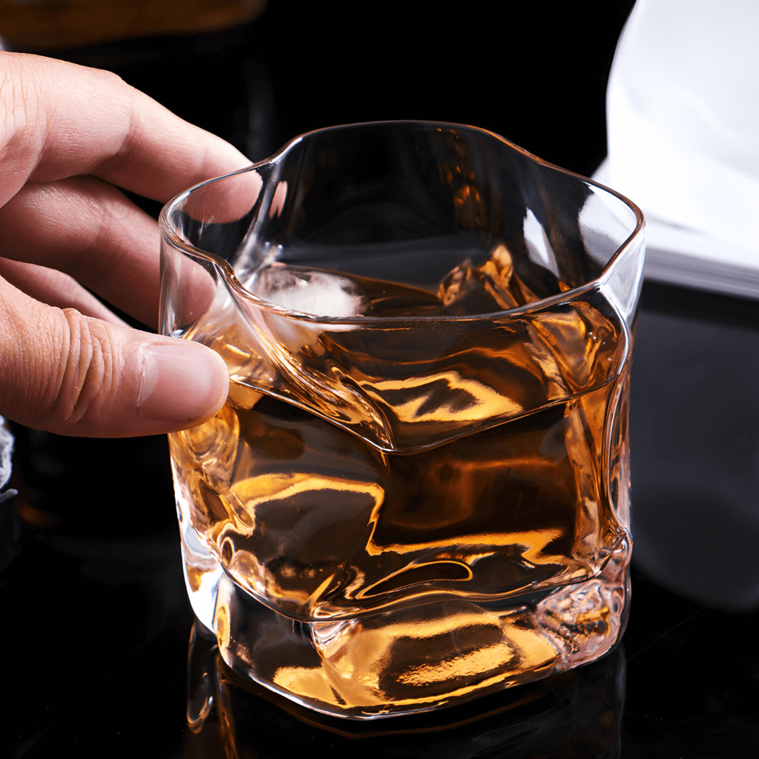 Hand holding faceted crystal whiskey glass with amber liquor and ice