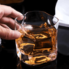 Hand holding faceted crystal whiskey glass with amber liquor and ice