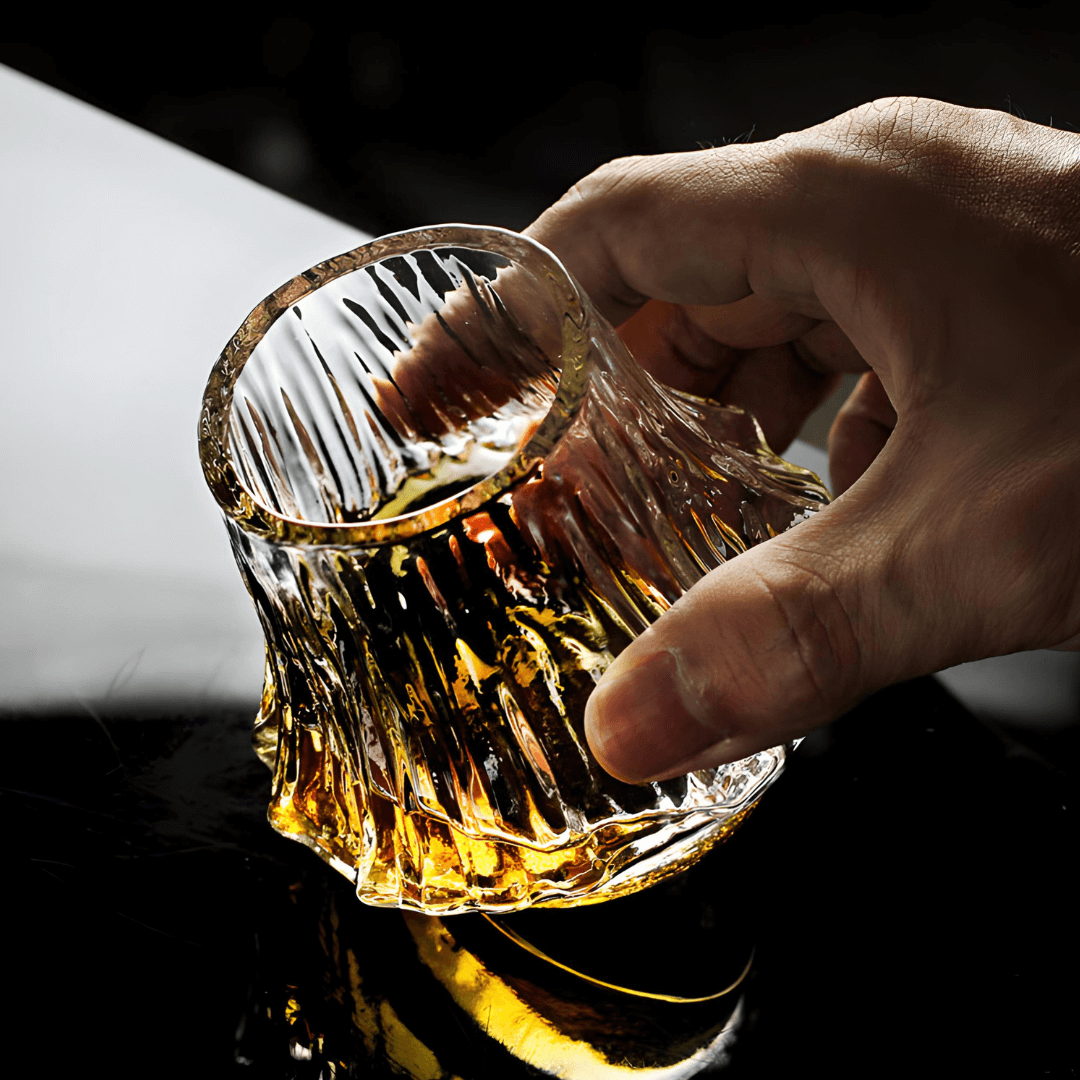 Japanese crystal whisky glass held by hand, amber whisky pooled in faceted bottom