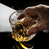 Japanese crystal whisky glass held by hand, amber whisky pooled in faceted bottom