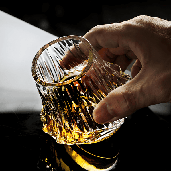 Japanese crystal whisky glass held by hand, amber whisky pooled in faceted bottom