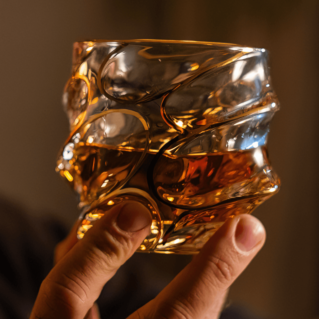 Japanese crystal whisky glass with gold line swirl pattern, held up