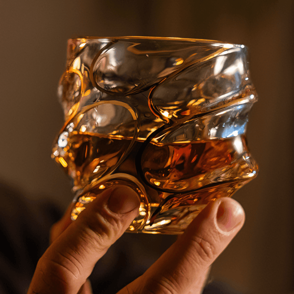 Japanese crystal whisky glass with gold line swirl pattern, held up