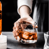 Hand pouring amber whisky into a faceted crystal whiskey glass