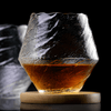 Faceted crystal whisky glass with amber liquid on wood coaster, angled view