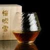 Textured crystal whisky glass with amber liquid inside and faceted irregular shape