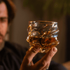 Gold-accented crystal whisky glass with swirling line cutout, held in hand