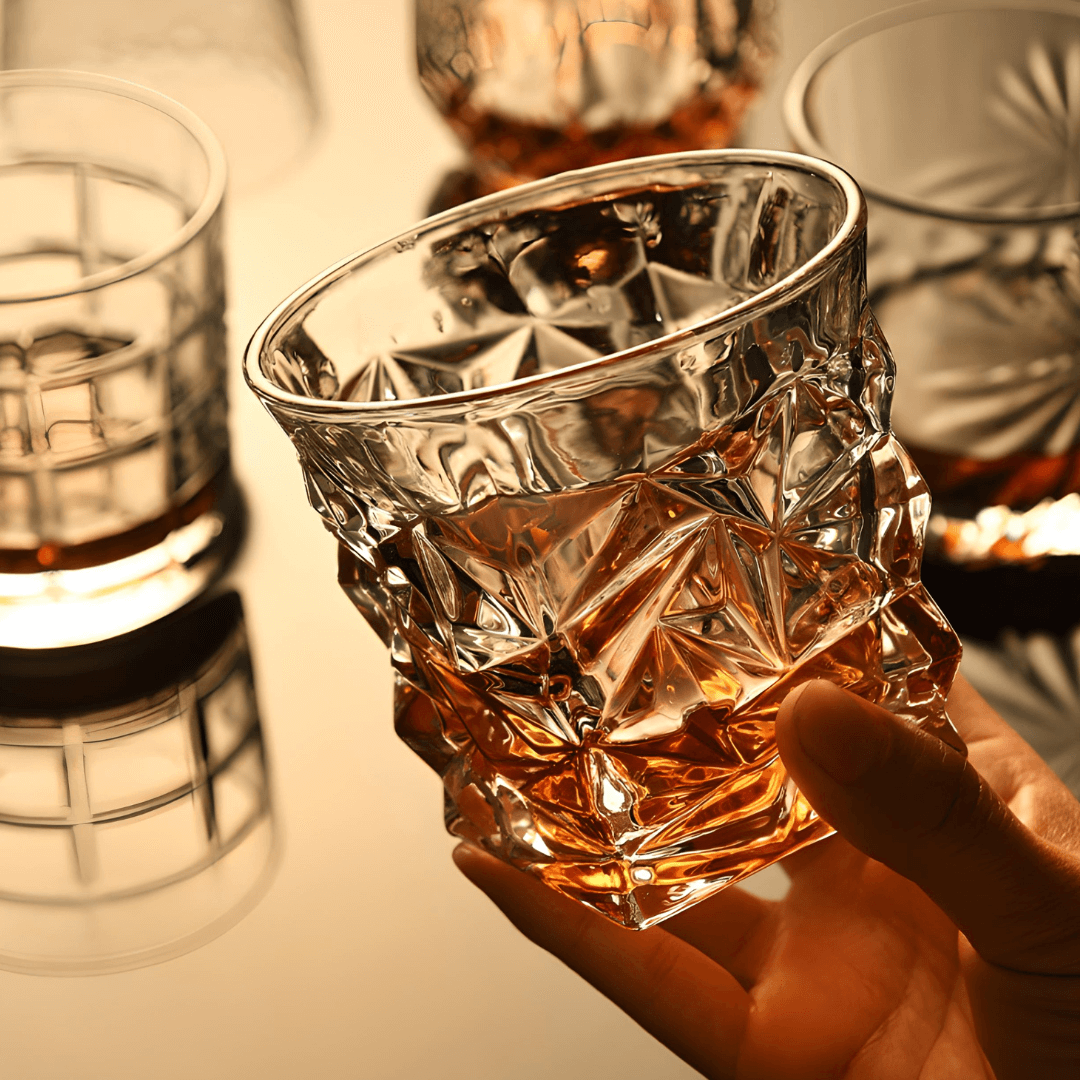 Hand holding a clear faceted Japanese crystal whisky tumbler with amber reflections