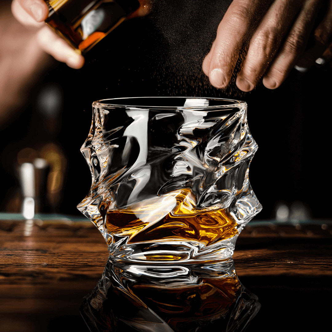 Crystal whisky glass with amber liquid, pour in progress on a wooden surface
