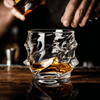 Crystal whisky glass with amber liquid, pour in progress on a wooden surface