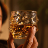 Gold-toned crystal whisky glass with swirling line pattern and faceted texture