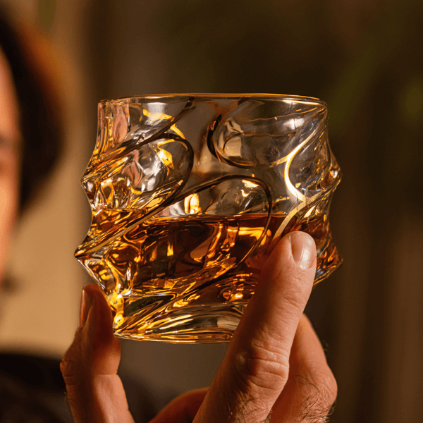 Gold-toned crystal whisky glass with swirling line pattern and faceted texture