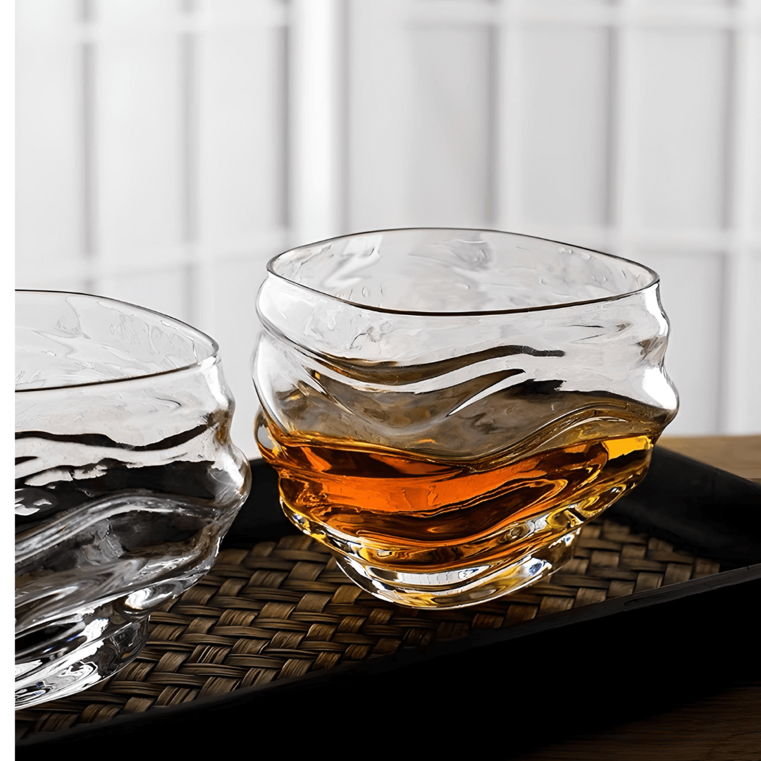 Two crystal whisky glasses on woven surface, each with amber liquid and ripples.