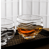 Two crystal whisky glasses on woven surface, each with amber liquid and ripples.