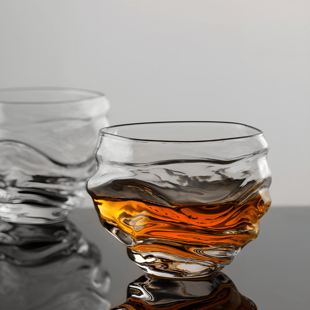Crystal whisky glass with amber liquid, wavy rim and faceted sides.