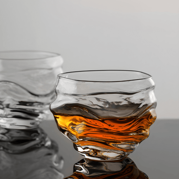 Crystal whisky glass with amber liquid, wavy rim and faceted sides.