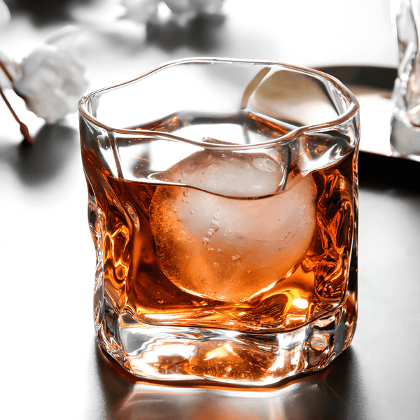 Faceted crystal whiskey glass with amber drink and ice, viewed from above