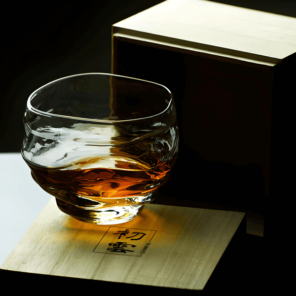Crystal whisky glass with amber liquid on a light wooden box with markings.