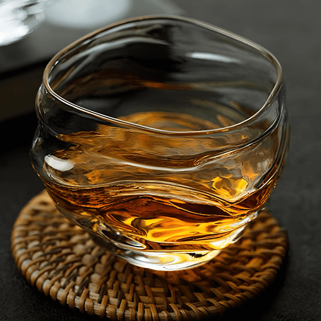 Crystal whisky glass holding amber whiskey, curved ripples visible in glass.