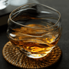 Crystal whisky glass holding amber whiskey, curved ripples visible in glass.