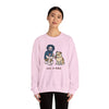 Light pink crewneck sweatshirt with front cartoon graphic; worn by a female model