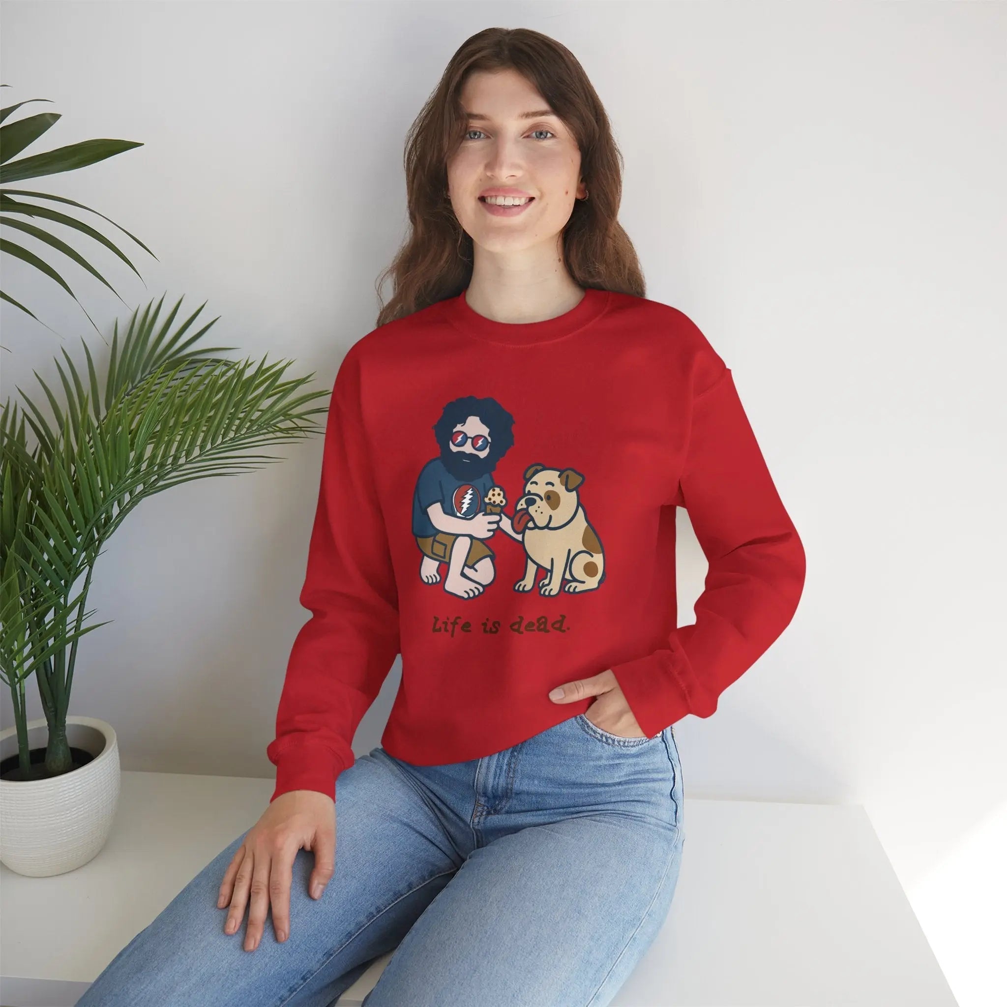 Red crewneck sweatshirt with front cartoon graphic; worn by a seated female model