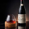 Crystal wine glass on round wooden coaster next to a red wine bottle