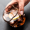 Gold Hoshi whisky glass with gold rim, hand holding amber-tinted crystal with ice