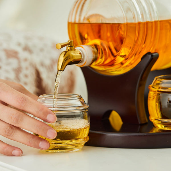 Whiskey decanter spigot pouring into a small amber glass jar on the tray