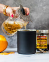 Dark insulated whiskey lowball tumbler receiving whiskey from a glass pitcher