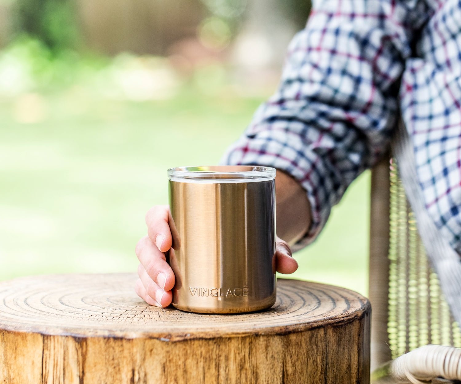 Gold insulated whiskey lowball tumbler held on top of a wooden stump