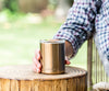 Gold insulated whiskey lowball tumbler held on top of a wooden stump