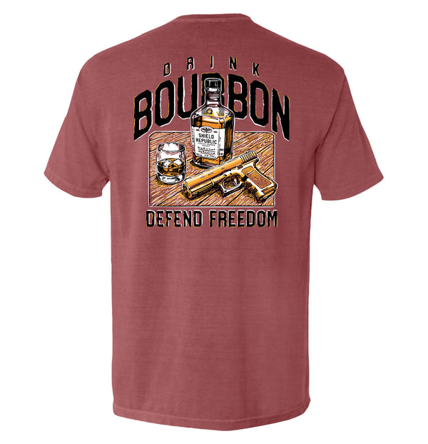 Rust-red T-shirt with back graphic: bourbon bottle, DRINK/BOURBON text, DEFEND FREEDOM