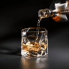 Gold-rim whisky glass with amber liquor being poured into faceted tumbler