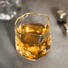 Gold-rim crystal whisky tumbler with amber drink, angled view