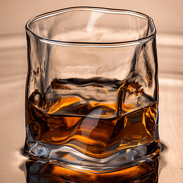Faceted crystal whiskey glass with amber drink and ice cubes