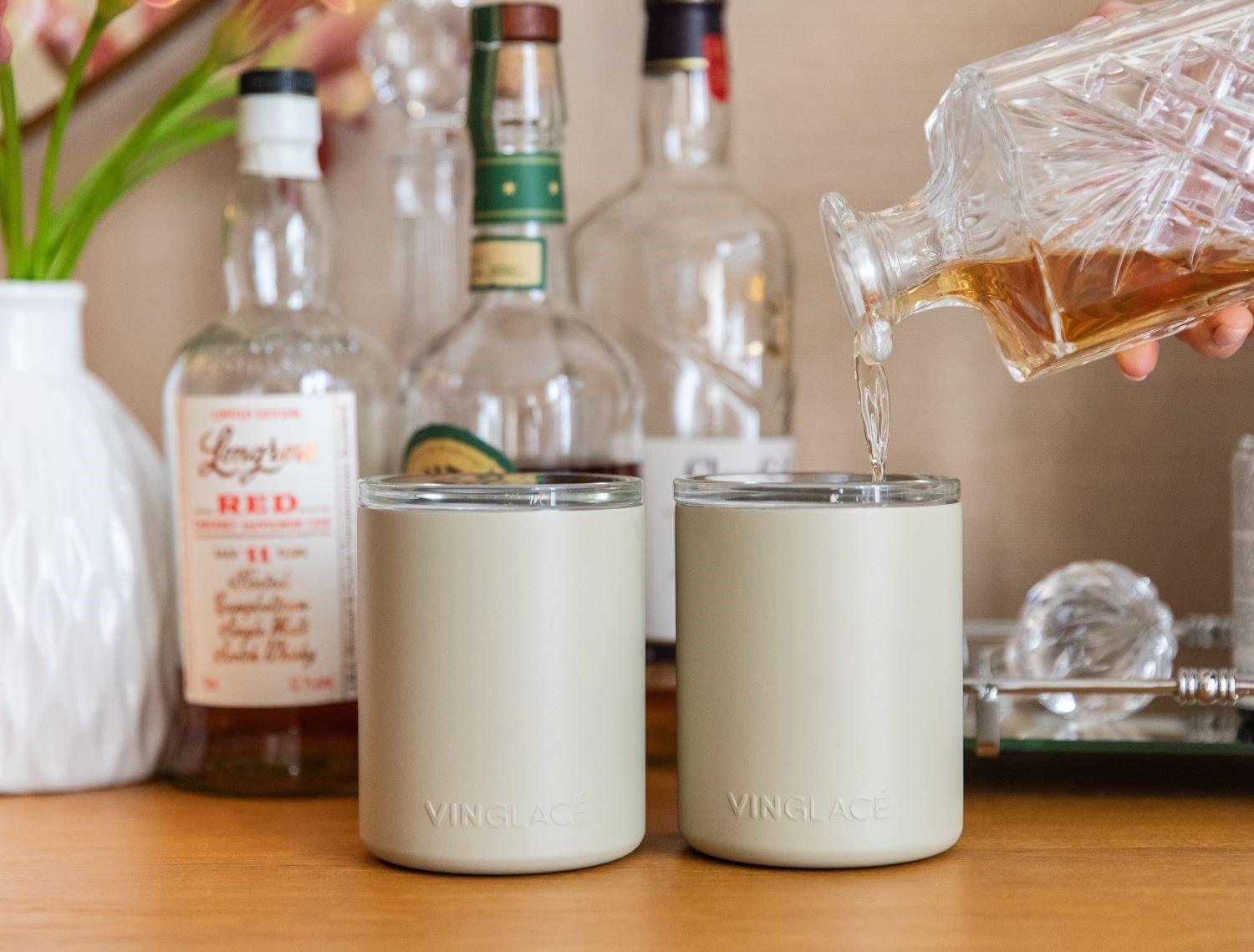 Two white glass-lined lowball whiskey tumblers with a hand pouring whiskey
