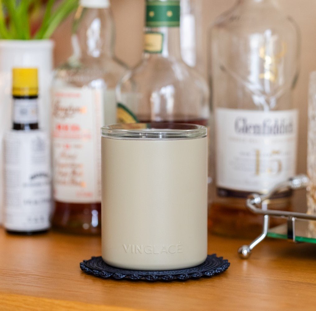 White insulated whiskey lowball tumbler on a table with bottles in background