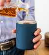 Navy glass-lined lowball whiskey tumbler with whiskey being poured into the cup