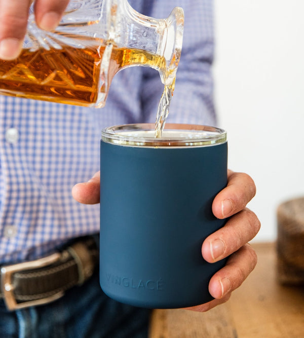 Navy glass-lined lowball whiskey tumbler with whiskey being poured into the cup