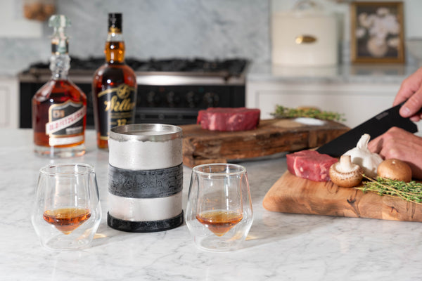 Double-walled glass tumbler with steel sleeve, amber drink being poured