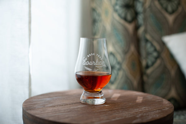 Stemmed bourbon tasting glass with amber liquid on wooden barrel lid