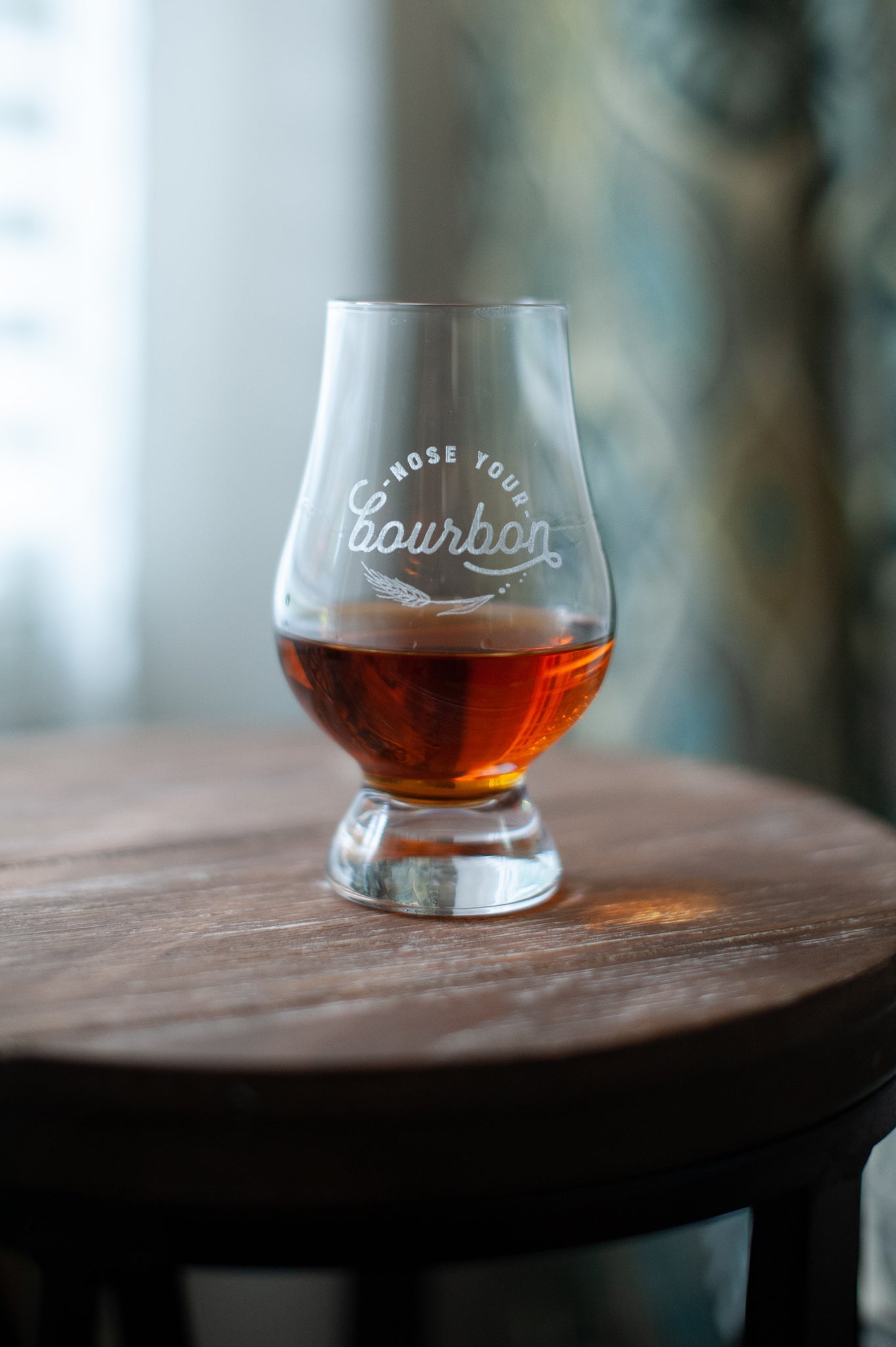 Engraved bourbon tasting glass with amber liquid on round wooden table