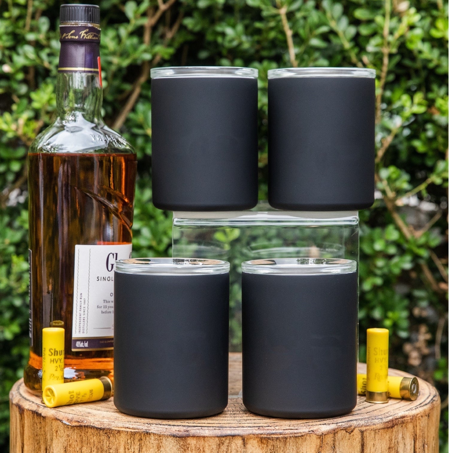 Set of four dark insulated whiskey lowball tumblers on a wood outdoor stump